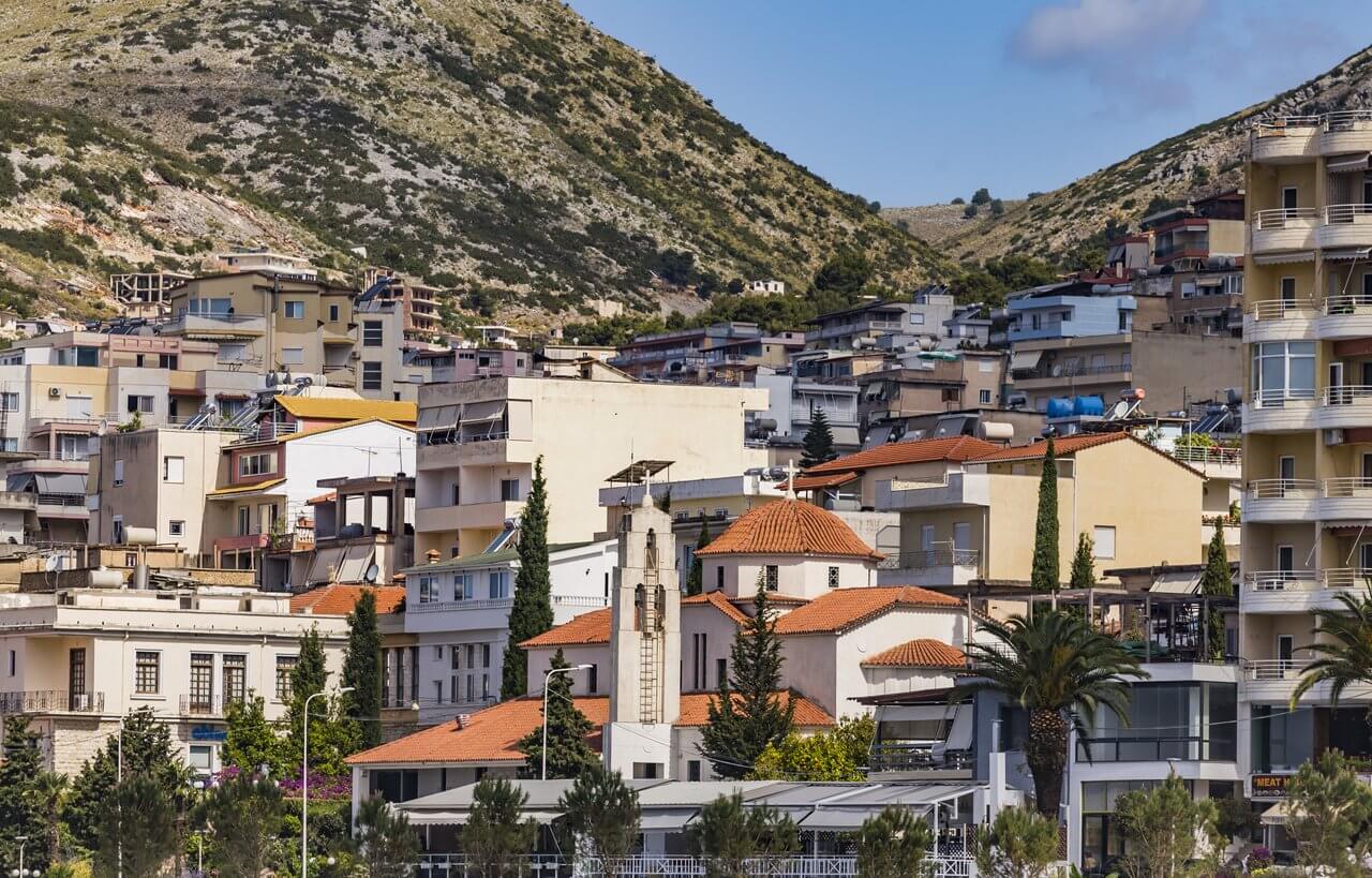 View of Saranda town houses and orthodox church bell tower on background of Albanian mountains.