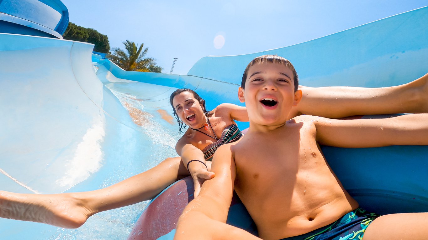 Mother and son speeding down fast on a water slide.