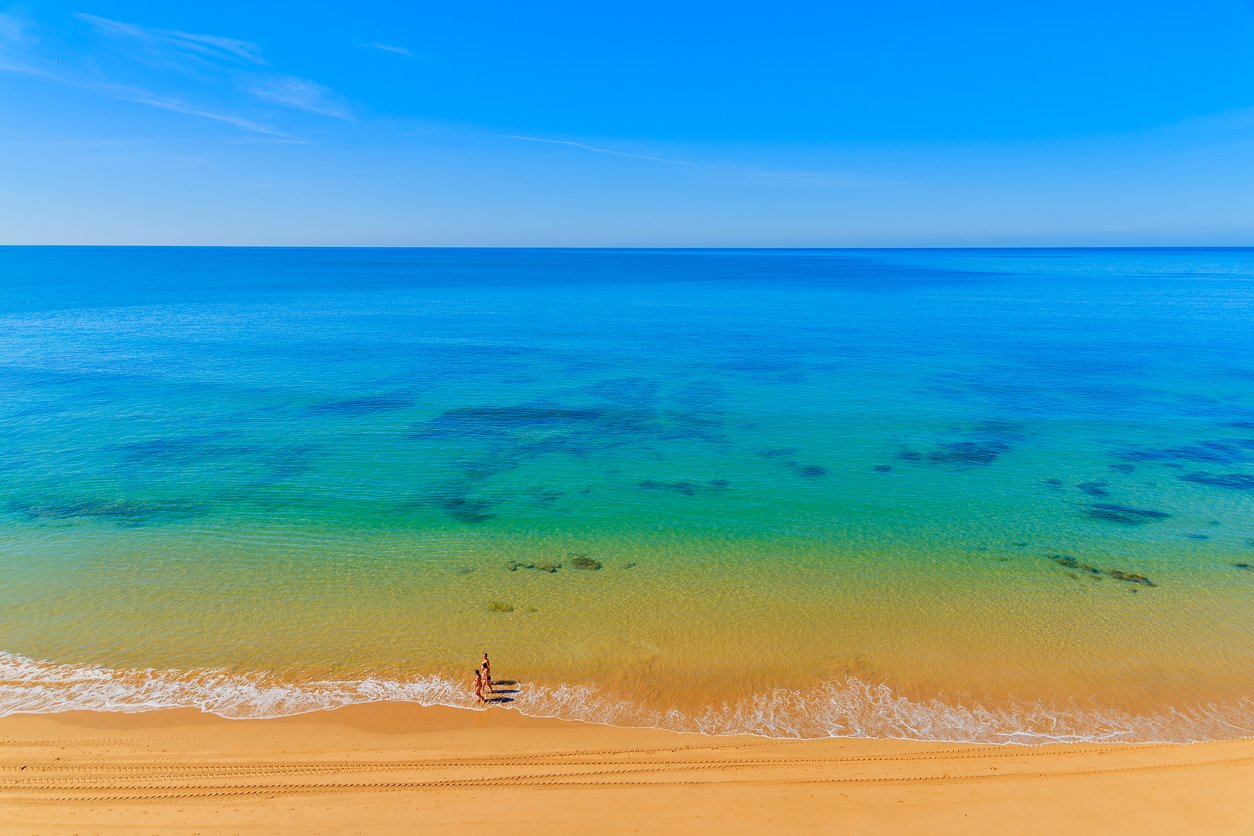 Three women walking on Praia da Rocha beach along ocean in Portimao town, Algarve region, Portugal