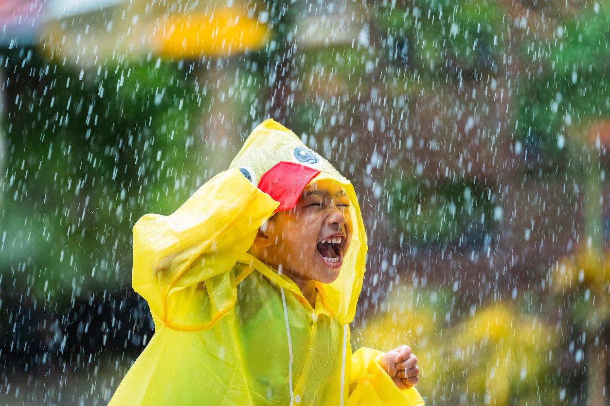 Asian boy wearing a raincoat outside the house. He is playing in the rain.