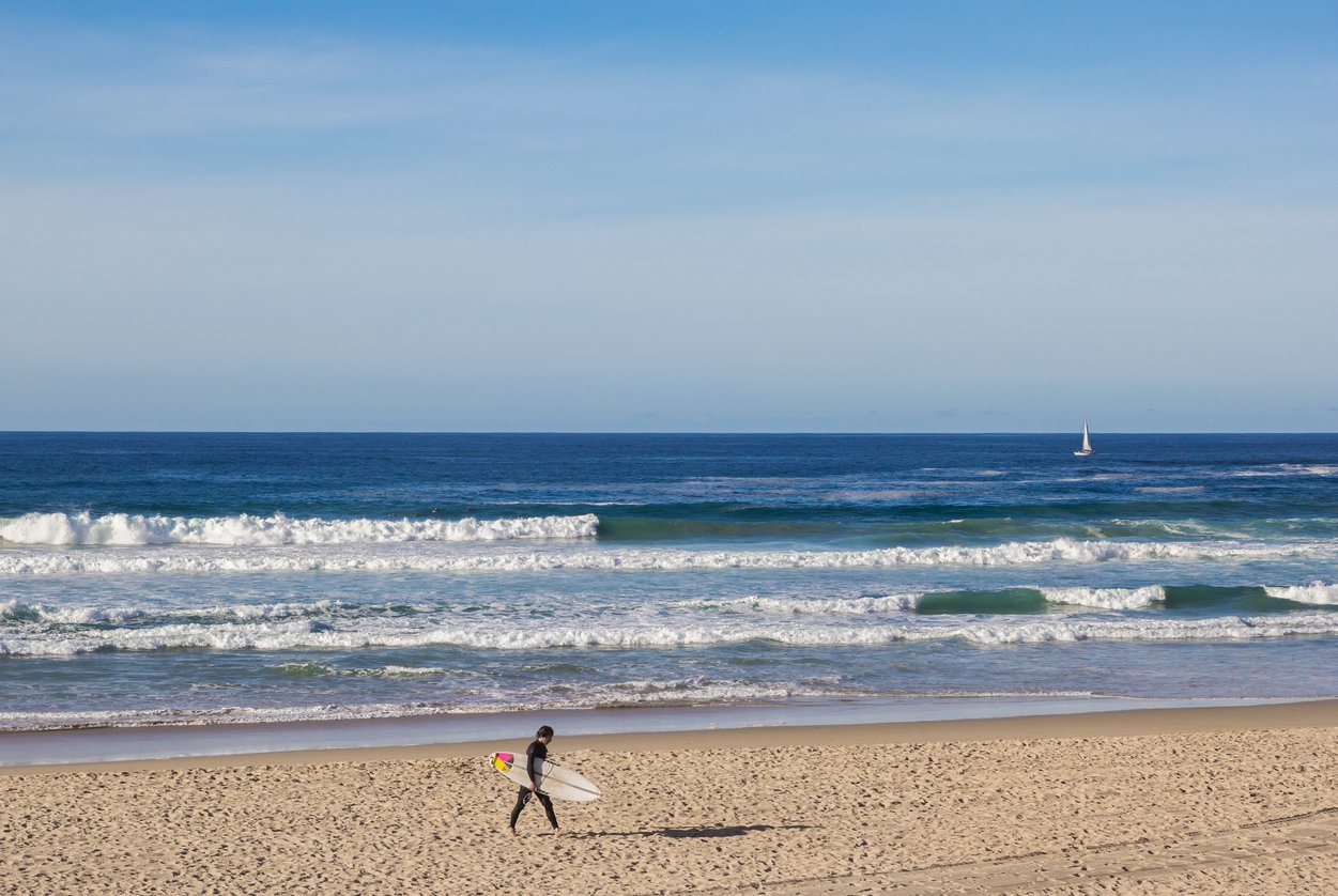 Surfeur avec planche de surf marchant sur la plage de Zurriola à Saint-Sébastien